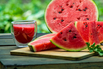 Delicious watermelon  outdoors wooden  table, GREEN  natural background sunny day, Heap,  Fresh ripe red, leaf, summer sunny garden juice drink organic sweet fruit, vegan food Tasty sliced board plate