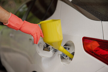 The man keeps a can for pouring gasoline from the canister into the car. Yellow watering can in the fuel holes. Gasoline collapse. Alternative fuelling method