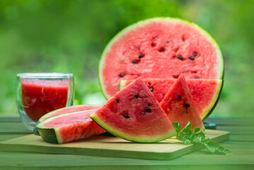 Delicious watermelon  outdoors wooden  table, GREEN  natural background sunny day, Heap,  Fresh ripe red, leaf, summer sunny garden juice drink organic sweet fruit, vegan food Tasty sliced board plate