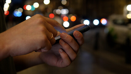 Close up of hands using smartphone at night on busy city street, concept of searching or using social network.