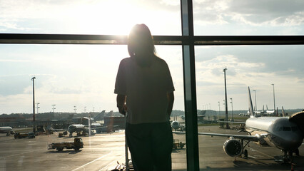 Random young passenger with a suitcase stands and watches the preparation of the planes while waiting to board the plane.