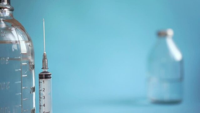 vaccination concept, foreground syringe and beaker with saline close-up, glass vial on blue blure background. horizontal video copy space tracking focus