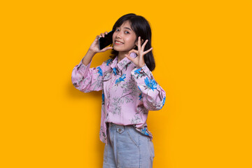 happy young asian beautiful woman using mobile phone isolated on yellow background
