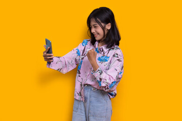 happy young asian beautiful woman using mobile phone isolated on yellow background
