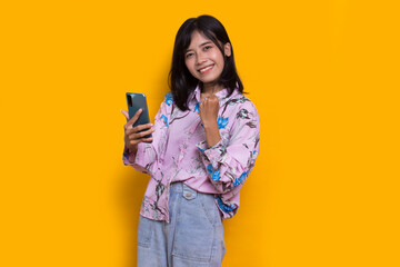 happy young asian beautiful woman using mobile phone isolated on yellow background
