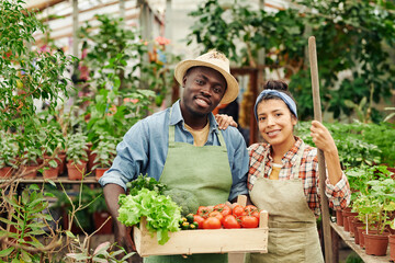 Horizontal medium portrait of modern ethnically diverse couple owning farm standing in greenhouse smiling at camera