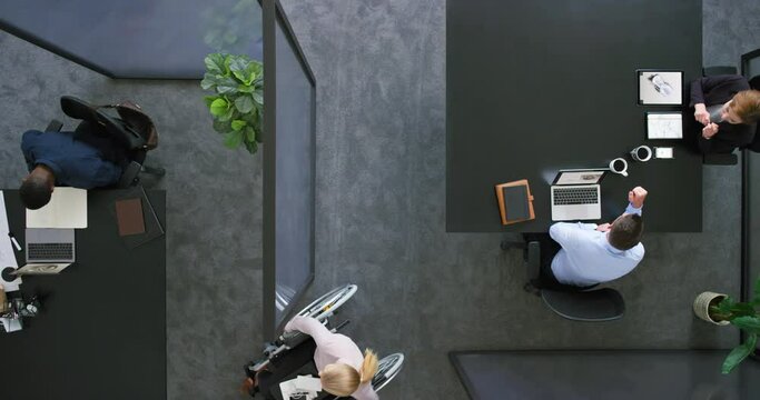 Disabled business manager in wheelchair using laptop and paperwork to talk, plan and brainstorm with team of colleagues. Corporate professionals discussing strategy in accessible and inclusive office