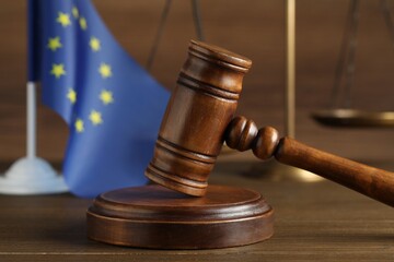 Judge's gavel, scales of justice and European Union flag on wooden table, closeup