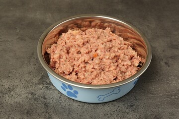 Wet pet food in feeding bowl on grey stone background