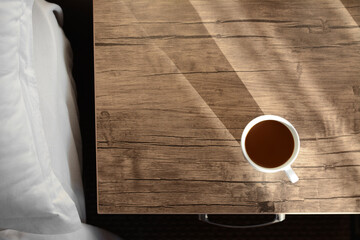 Cup of coffee on wooden night stand near bed in morning, top view. Space for text