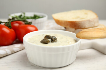 Creamy caper sauce in bowl on white wooden table, closeup