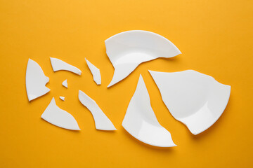 Pieces of broken ceramic plate on orange background, flat lay