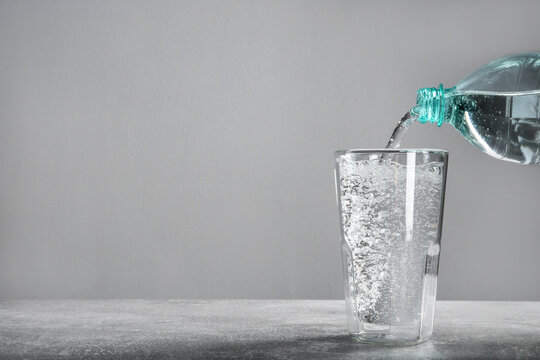 Pouring Soda Water From Bottle Into Glass On Grey Table. Space For Text