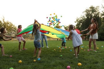 Group of children and teacher playing with rainbow playground parachute on green grass. Summer camp activity - Powered by Adobe