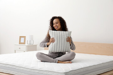 Happy young African American woman hugging pillow on bed with comfortable mattress at home