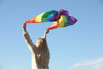 Woman holding bright LGBT flag against blue sky