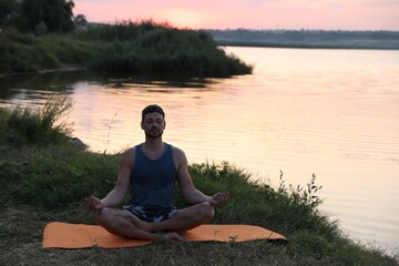Fototapeta na wymiar Man meditating near river in twilight. Space for text