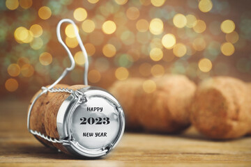 Cork of sparkling wine and muselet cap with engraving Happy 2023 New Year on wooden table against...