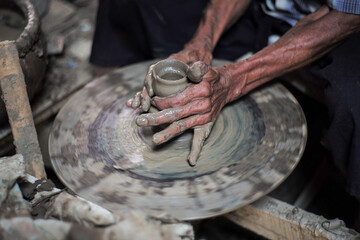 Selective focused on the dirty wrinkled skin hands of old man molding the clay work on the spinning...