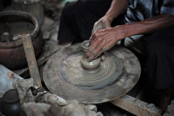 Selective focused on the dirty wrinkled skin hands of old man molding the clay work on the spinning wheel for making the traditional jar