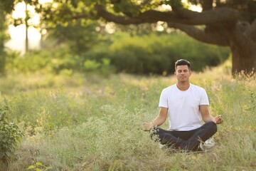 Man meditating on green grass in park, space for text - obrazy, fototapety, plakaty