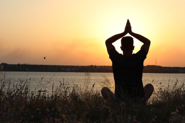 Man meditating near river at sunset, back view. Space for text