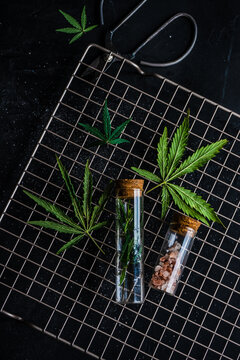 Overhead view of marijuana leaves and pink Himalayan salt in glass jars on a metal cooling rock