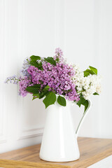 Beautiful lilac flowers in vase on wooden table near white wall