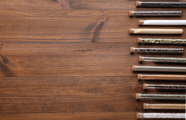 Test tubes with various spices on wooden table, flat lay. Space for text