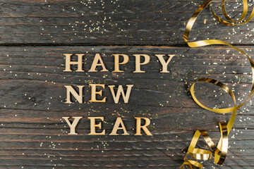 Happy new year inscription made with wooden letters decorated festive golden serpentine on wooden...