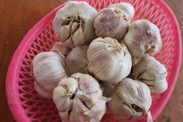 Bunch of garlic in a pink basket. Vitamin healthy food spice image. Spicy cooking ingredient picture. Pile of white garlic heads. White garlic head heap top view
