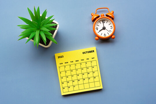 October 2023 calendar on adhesive note with alarm clock set at 8 o'clock.