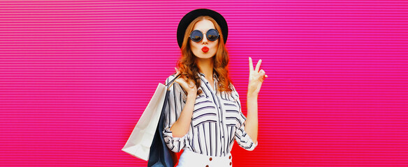 Portrait of beautiful young woman with shopping bags blowing her lips sending air kiss wearing...