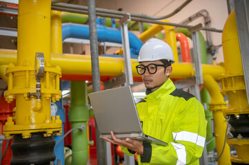 Asian engineer wearing glasses working in the boiler room,maintenance checking technical data of heating system equipment,Thailand people