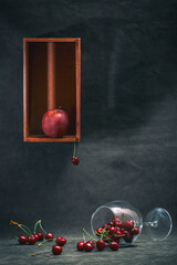 Still life with ripe apples and red cherries in a fallen glass