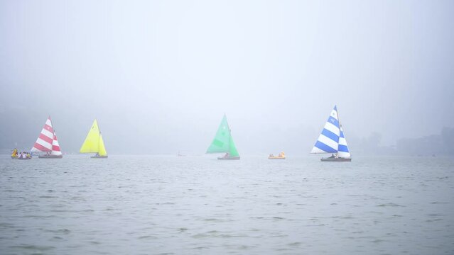 four colorful sailboats lost in the haze fog with smaller pedal row boats floating around on the cloudy naini jheel in nainital lake in uttarakhand India a popular tourist destination