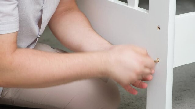 The furniture assembler assembles the bed, twists the screws on the wooden parts.
