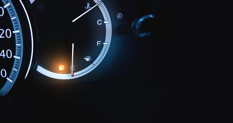 An indicator for low fuel is illuminated on a dashboard of a car with copy space