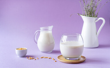 Vegan healthy pea milk in glass and jar, pea seeds and white jug with lavender. Lilac background. Copy space