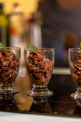 A close up portrait of a few glass cups full of delicious chocolate mousse with a mint leaf on top of them for some freshness standing on a cooking plate ready to be served and eaten.