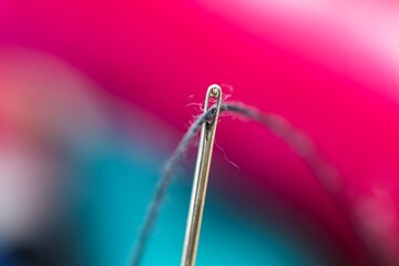 A colorful close up portrait of a needle with a black thread running through the eye of the needle. The metal sewing equipment has a hole in it to put wires through. - Powered by Adobe