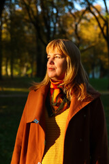 Defocus portrait of middle aged Caucasian blonde woman in autumn park. Bright stylish woman in...