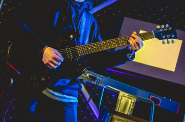 Closeup of young latino guitarist and keyboardist with hoodie and black guitar playing live in a concert under yellow and blue lights in the night