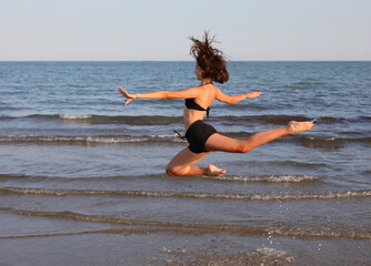 athletic girl performing a difficult rhythmic gymnastics jump called CIRCLE JUMP by the sea