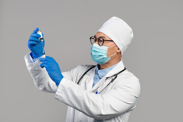 Busy serious adult korean doctor in white coat, glasses and gloves take vaccine into syringe