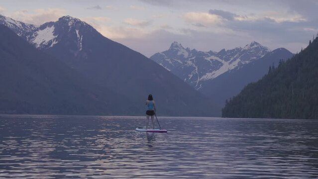 Adventurous Woman Paddle Boarding in a Lake around Canadian Mountain Landscape. Chilliwack Lake, British Columbia, Canada. Adventure Sport Travel