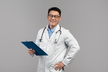 Portrait of happy confident adult asian doctor in white coat, glasses with stethoscope and tablet...