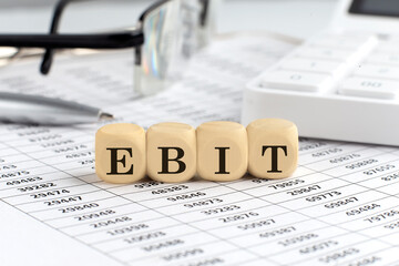 wooden cubes with the word EBIT on a financial background with chart, calculator, pen and glasses, business concept.