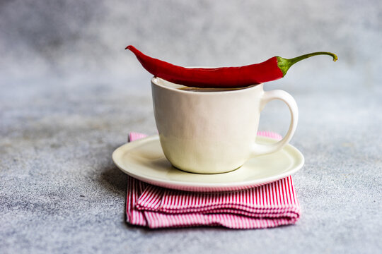 Close-Up Of A Cup Of Coffee With A Red Chilli Pepper On A Folded Napkin