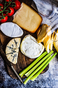 Overhead view of assorted French cheeses with tomatoes, celery and bread on a  chopping board